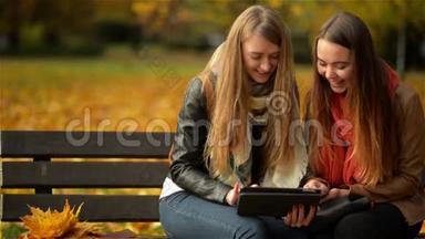 两个有趣的快乐年轻女孩朋友坐在长凳上用平板电脑。 女人在Pad电脑上嬉笑<strong>打闹</strong>